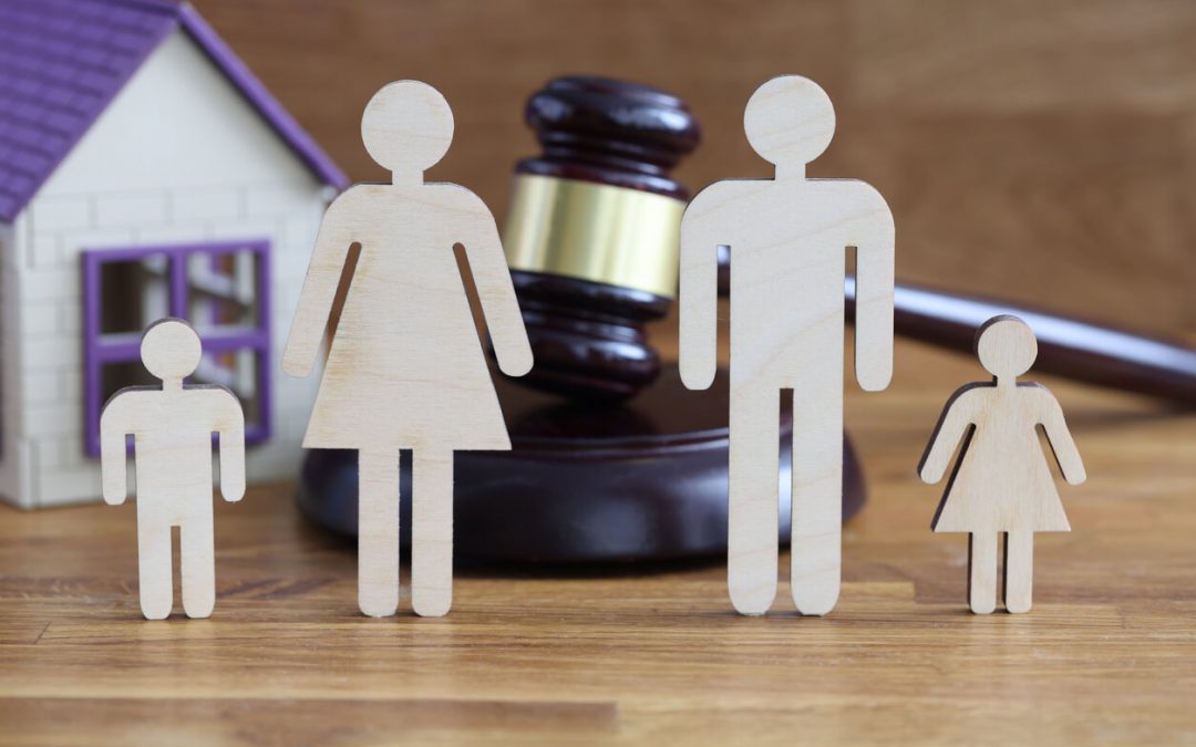 Wooden figurines of parents and children stand on table near toy house and judges hammer. Division of property in case of divorce concept